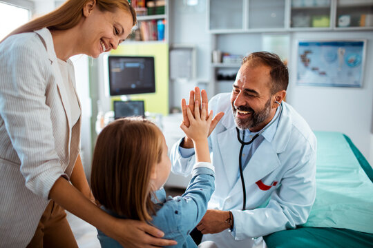 Smiling pediatrician high-fives child during checkup in clinic with mother