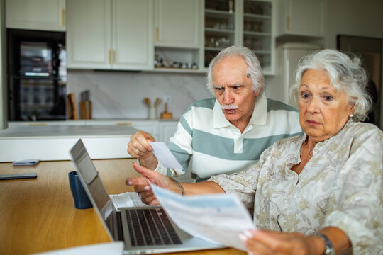 Senior couple reviewing household bills on laptop at kitchen table
