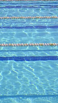 Crystal clear blue water in a swimming pool gently rippling in the summer sun, showing lane lines for competition and reflections on the tiled bottom, creating a refreshing and relaxing background