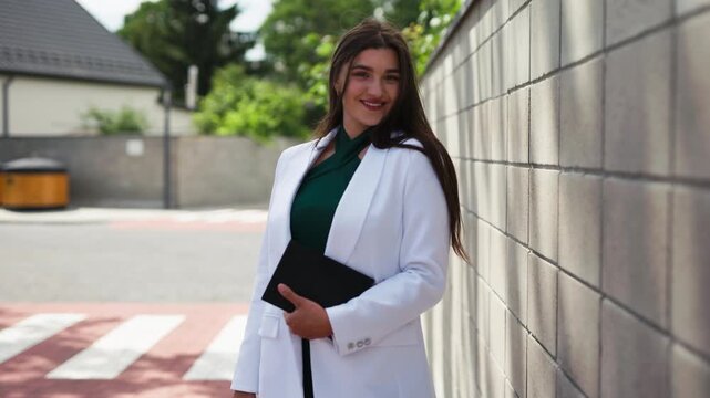 Beautiful young business woman standing near stone wall outdoors with notebook, slow motion