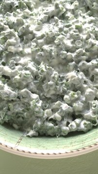 Close-up of a bowl of dip made with Greek yogurt, finely chopped chives, and salt. A quick, healthy dip, potato sauce, or side dish for grilled dishes. Table spin, vertical video.