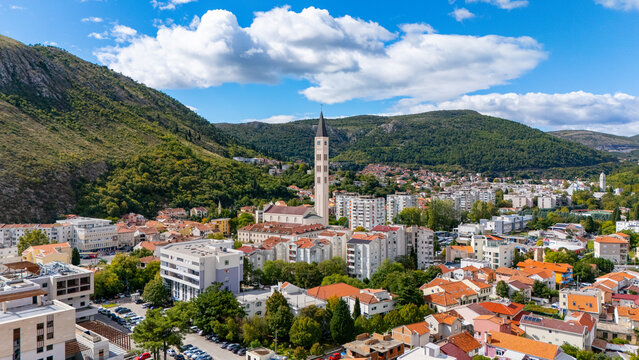 Aerial view of the Franciscan Church of St. Peter and Paul bell tower rising above the urban landscape of Mostar, with red-tiled rooftops in Mostar, Federation of Bosnia, Bosnia and Herzegovina.