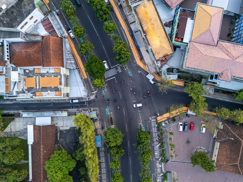 Aerial view of a busy street intersection surrounded by urban buildings with orange rooftops, lush green trees, and paved roads in Klaten, Central Java, Indonesia.