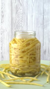 Lacto-fermentation of green beans: a jar containing yellow-streaked beans, approaching the final stage of fermentation. Healthy, high-protein, vegan food. Vertical video, copy space, table spin.