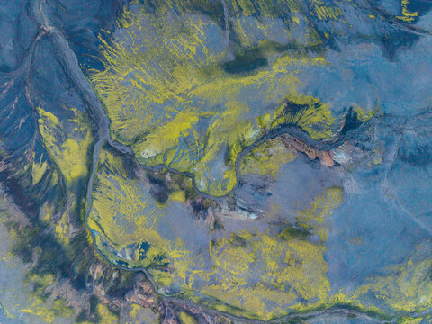Aerial view of volcanic landscape with vibrant green moss covering dark lava fields and a winding river in Iceland.