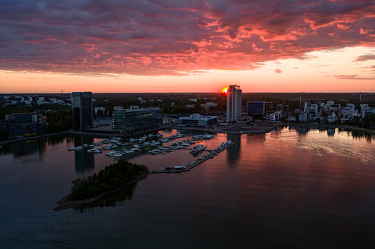 Aerial view of Keilaniemi with modern office buildings and a marina on the waterfront under a vibrant sunset sky in Espoo, Uusimaa, Finland.