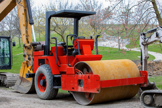 A red steamroller with rusty roller drum parked on site