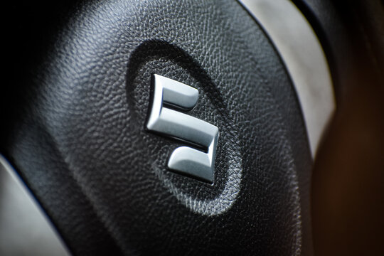 KERALA, INDIA - JULY 20, 2020: Close up of metallic chrome Suzuki logo on leather car steering wheel with selective focus.