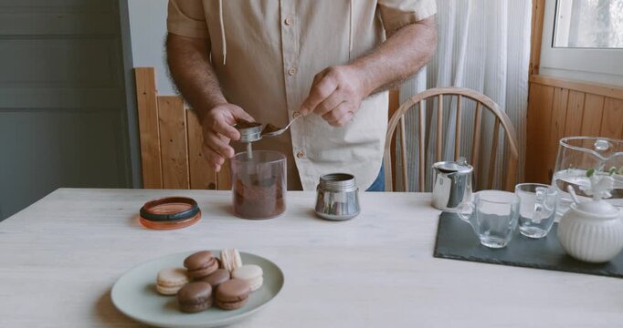 Man making coffee at home, putting ground coffee into moka pot. Preparation home coffee, morning ritual, coffee brewing process.