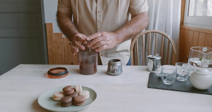 Man making coffee at home, putting ground coffee into moka pot. Preparation home coffee, morning ritual, coffee brewing process.