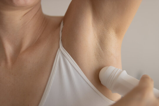 Woman applying roll-on antiperspirant to her underarm, maintaining personal hygiene and skin health, focusing on daily body care routine for freshness and confidence