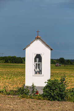 Small White Wayside Shrine With Cross In A Rural Field Under Blue Summer Sky