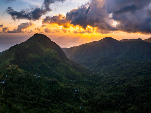 Aerial view of the lush green mountains at Lahangan Sweet during a vibrant sunset with dramatic clouds and golden light over the valley in Kecamatan Abang, Bali, Indonesia.