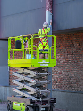 Construction Worker Painting Steel Support Column from Elevated Scissor Lift at Building Exterior Site