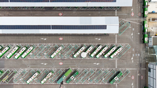 Aerial view of a modern electric bus depot with rows of green buses parked in an organized urban transport facility, San Donato Milanese, Lombardy, Italy.