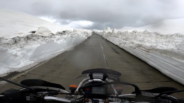 POV motorcycle ride through towering snow walls on Zagari Pass in Svaneti, Georgia. Epic mountain road adventure with breathtaking alpine scenery and a unique summer riding experience