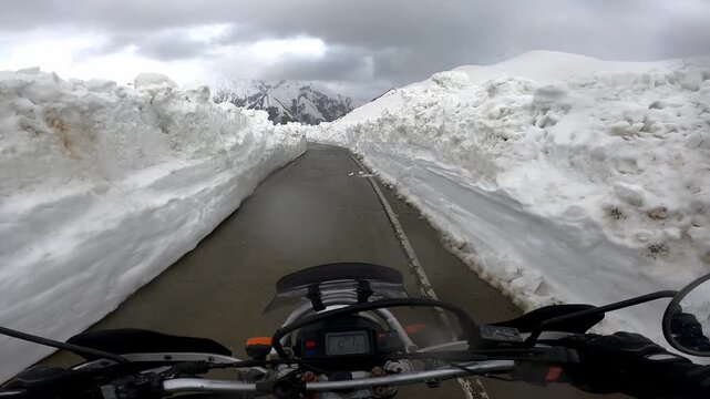 POV motorcycle ride through towering snow walls on Zagari Pass in Svaneti, Georgia. Epic mountain road adventure with breathtaking alpine scenery and a unique summer riding experience