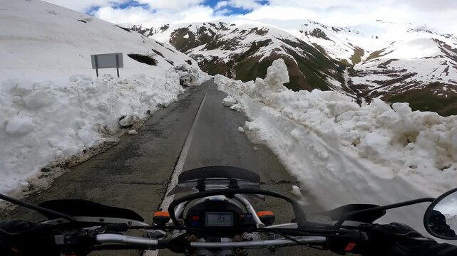 POV motorcycle ride through towering snow walls on Zagari Pass in Svaneti, Georgia. Epic mountain road adventure with breathtaking alpine scenery and a unique summer riding experience
