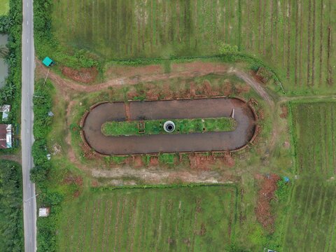 Overhead top-down drone shot showing a uniquely shaped oval dirt track or ground pattern surrounded by green paddy fields and countryside.