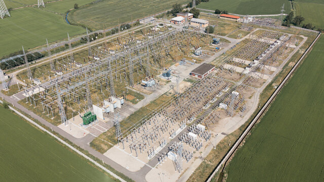Aerial view of the C.P. Lacchiarella electrical substation featuring high-voltage transformers and power lines surrounded by green agricultural fields in Badile, Lombardia, Italy.