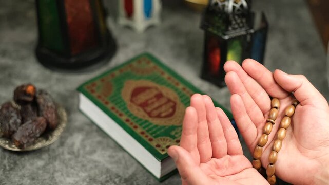 Hands Raised in Islamic Prayer With Tasbih Beside Quran and Dates