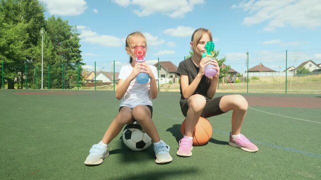 Girls Resting On Sports Balls And Drinking Outdoors
