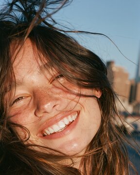 Young woman laughs with wind in her hair on city rooftop during golden hour