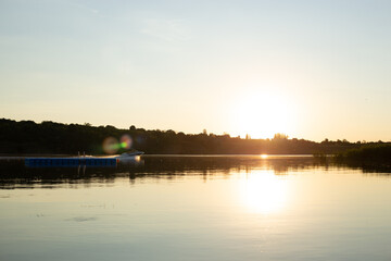 Naklejka premium Motorboat cruising across a calm lake at golden sunset with reflections