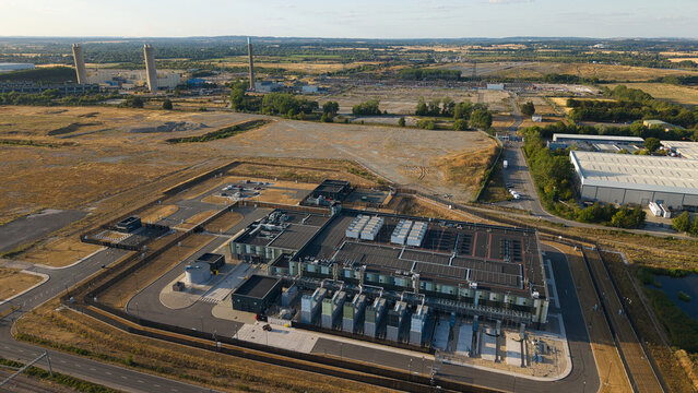 Aerial view of a hyperscale data center with cooling units and rooftop infrastructure, near Didcot Power Station cooling towers during golden hour in Didcot, England, United Kingdom.