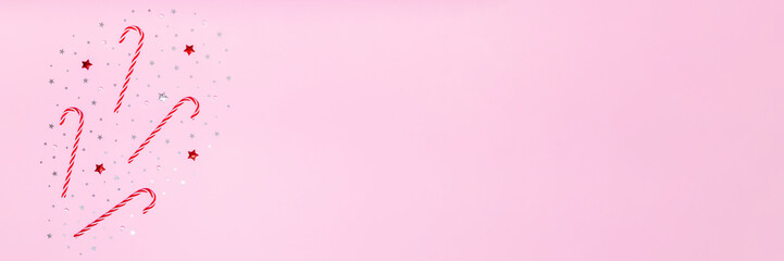 Pink holiday background with candy canes, red and silver stars on left side, leaving wide copy space for festive banners, sales, greetings and seasonal promo designs. © Iryna Budanova