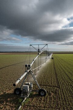 Large center pivot irrigation system waters young green crops on agricultural field. Automated machinery sprays liquid across wide rural farm under dark cloudy sky. Modern technology provides