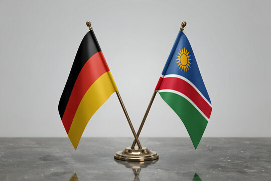 Small desktop flags of germany and rwanda crossed on a dark marble table in a blurred office room with a plain light grey wall background