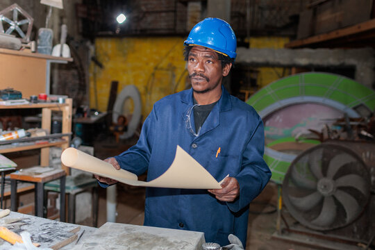 African worker stands at a construction site holding rolled plans