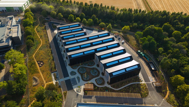Aerial view of the tech foundry 3 building at Harwell Science and Innovation Campus, featuring a sawtooth roof with solar panels and landscaped grounds in Didcot, England, United Kingdom.