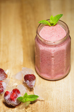 Fresh strawberry smoothie in glass jar with frozen berries and mint on table