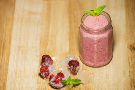 Fresh strawberry smoothie in glass jar with frozen berries and ice on table