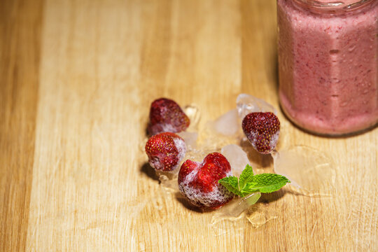Fresh frozen strawberries on ice near smoothie jar with copy space