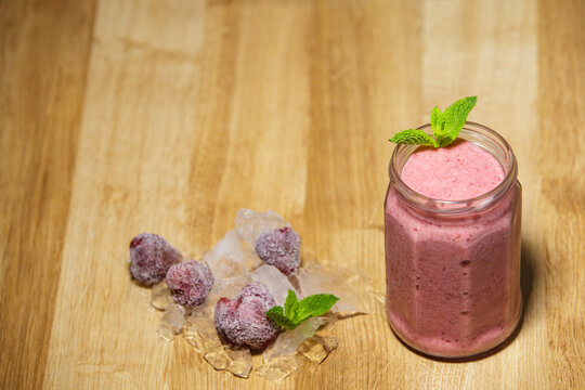 Fresh strawberry smoothie in glass jar with ice mint and berries on wooden table