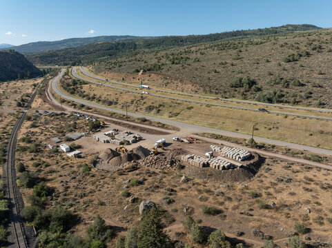 Aerial view of a construction site with piles of gravel, concrete blocks, and heavy machinery located near Interstate 70 and railroad tracks in Wolcott, Colorado, United States.
