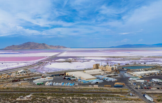 Aerial view of the salt processing facility with pink salt evaporation ponds, industrial buildings, and train cars near the Great Salt Lake in Grantsville, Utah, United States.