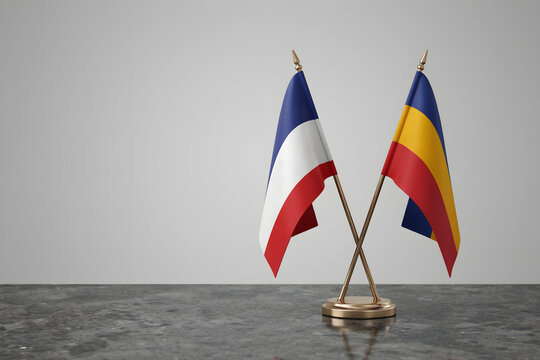 Small crossed desk flags of france and romania on a dark marble surface against a plain light gray background, for diplomatic meetings