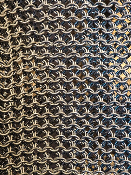 Close up of interlinked metal chainmail rings creating a detailed medieval armor texture. Seamless looking metallic pattern for historical and industrial design concepts.