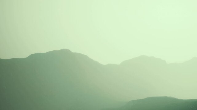 A mountain range is visible with some fog covering the peaks. The scene shows a soft light during early morning hours. The landscape appears calm and distant.