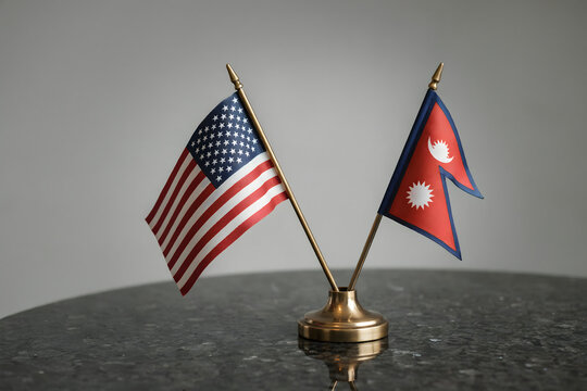 Small desk flags of the united states and nepal standing on a dark marble table against a plain grey background, for diplomatic meetings