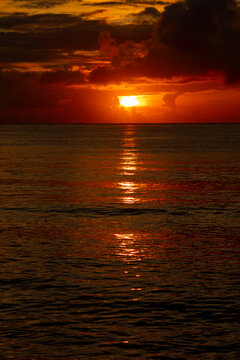 Vivid sun breaking through dark clouds over the ocean horizon with brilliant reflection.