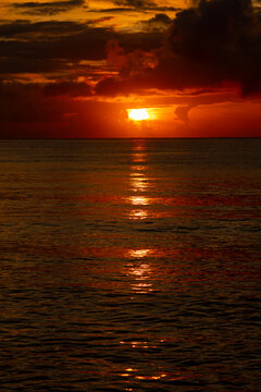 Vivid sun breaking through dark clouds over the ocean horizon with brilliant reflection.