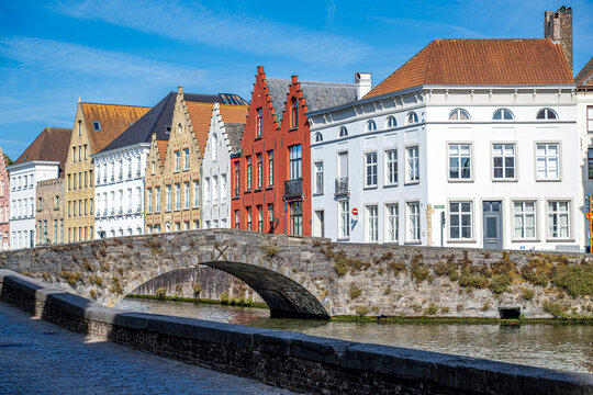 Historic stone bridge crossing a picturesque canal in Bruges, Belgium surrounded by colorful traditional Flemish buildings and preserved medieval urban architecture