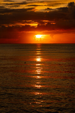 Vivid sun breaking through dark clouds over the ocean horizon with brilliant reflection.