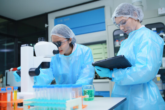 Laboratory Scientists Using Microscope and Tablet for Research Analysis