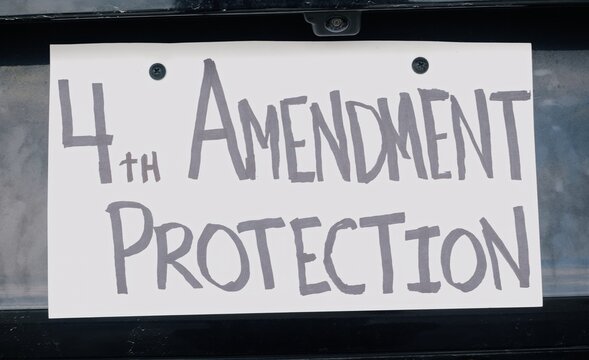 Man attaching protest license plates to vehicle using screwdriver, illustrating citizen pushback against ALPR surveillance - Fourth Amendment privacy
